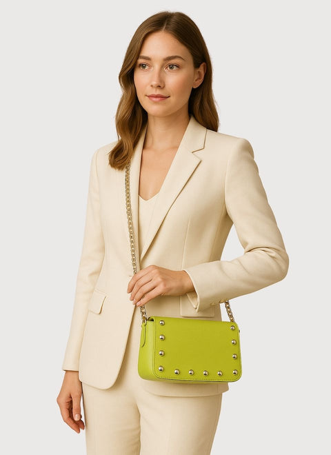 Modelo con  un bolso fiesta verde lima hecho a mano en nuestro taller con piel de máxima calidad y tachas plateadas. Un elegante bolso estilo baguette en un tono original y de tendencia, que puedes llevar al hombro o cruzado, gracias a su ligera cadena metálica de aluminio.