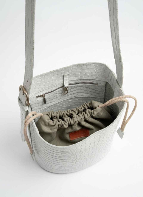 bolso de piel blanco visto desde arriba dónde se muestra el interior del bolso conuna bolsa fruncida de tela dóndee llevar cerradas las cosas y también es visible un bolsillo con cremallera