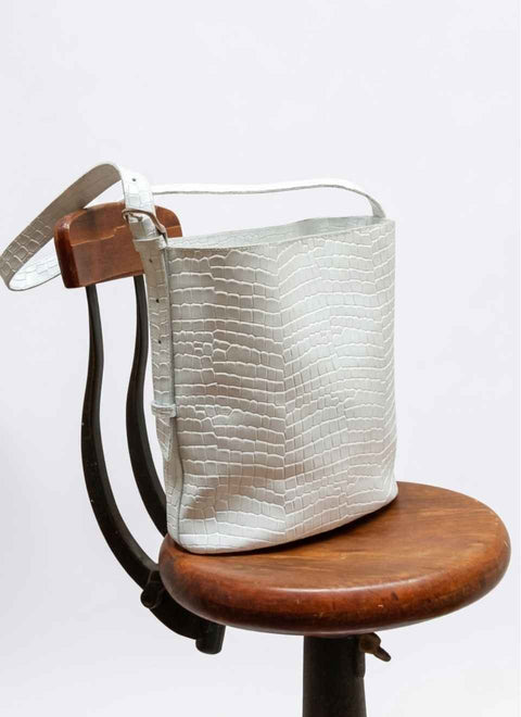 Bolso bucket de piel blanca grabada parallevar al hombro o cruzado, encima de una silla