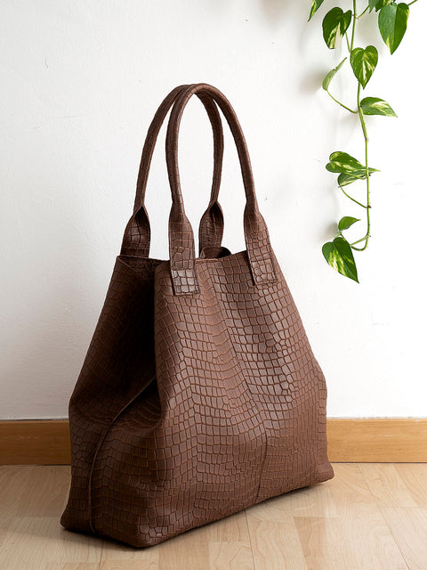 La foto muestra el bolso grande piel Marrón Maxi es formato compacto, que reduce el tamaño original gracias a unos  broches interiores. El bolso tiene dos asas y es de piel de vacuno en color marrón oscuro, con grabado efecto cocodrilo. 