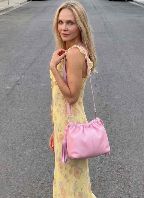 mujer con bolso rosa clar  vestida de fiesta, en piel. Ligero y actual, con flecos a los lados. Asa extraible, convertible en clutch. 