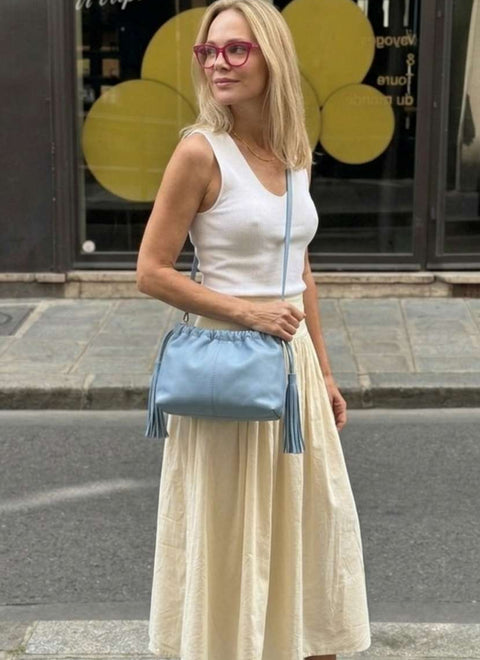 Modelo con un bolso de piel color azul claro, lo lleva en bandolera, y tiene flecos en los dos lados de la misma piel
