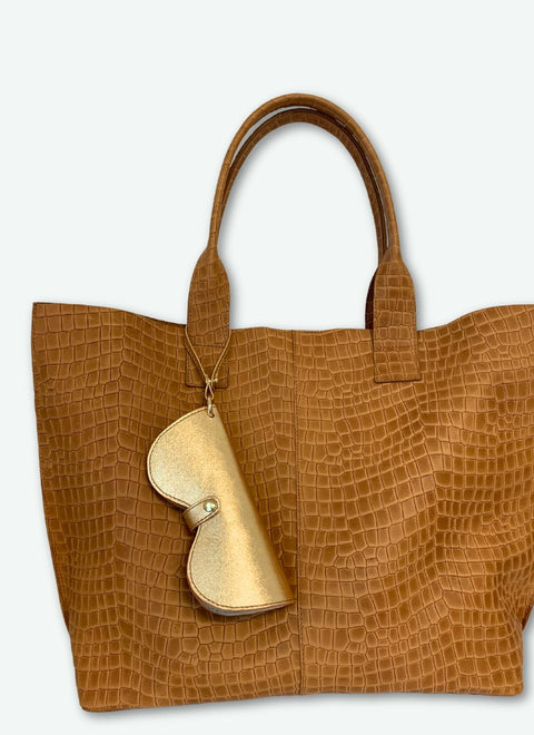 Funda de gafas dorada combinada con bolso color camel. Elegancia artesanal en tonos cálidos y metálicos.