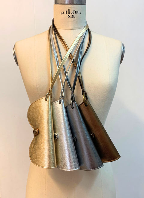 Fundas de gafas en dorado, plata, plomo y bronce colgando de un maniquí. Correas intercambiables para cuello o bolso.