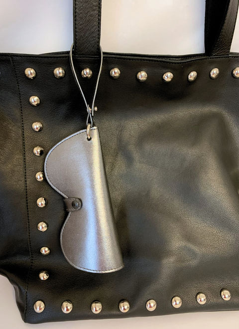 Funda plateada para gafas colgando de un bolso negro. Estilo chic y funcional para llevar tus lentes siempre a mano.