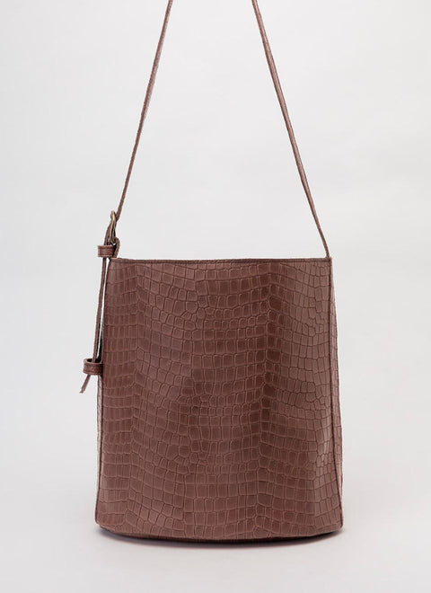 La foto muestra un bolso Cubo Piel Marrón Oscuro con el asa regulable, confeccionada en la misma piel.  La piel es de vacuno con un grabado efect cocodrilo. 