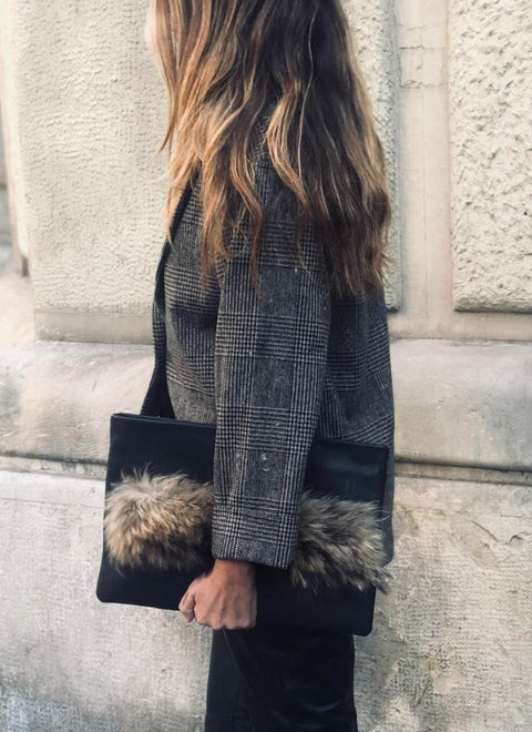 La foto muestra una mujer, probablemente una ejecutiva, que lleva una cartera de mano confeccionada artesanalmente en nuestro taller con piel y pelo natural. La cartera es grande y combina el color y la textura de la piel lisa con las tonalidades del asa de pelo que, en el lateral de la cartera, sirve de decoración y asidero para llevarla de una forma cómoda y original.